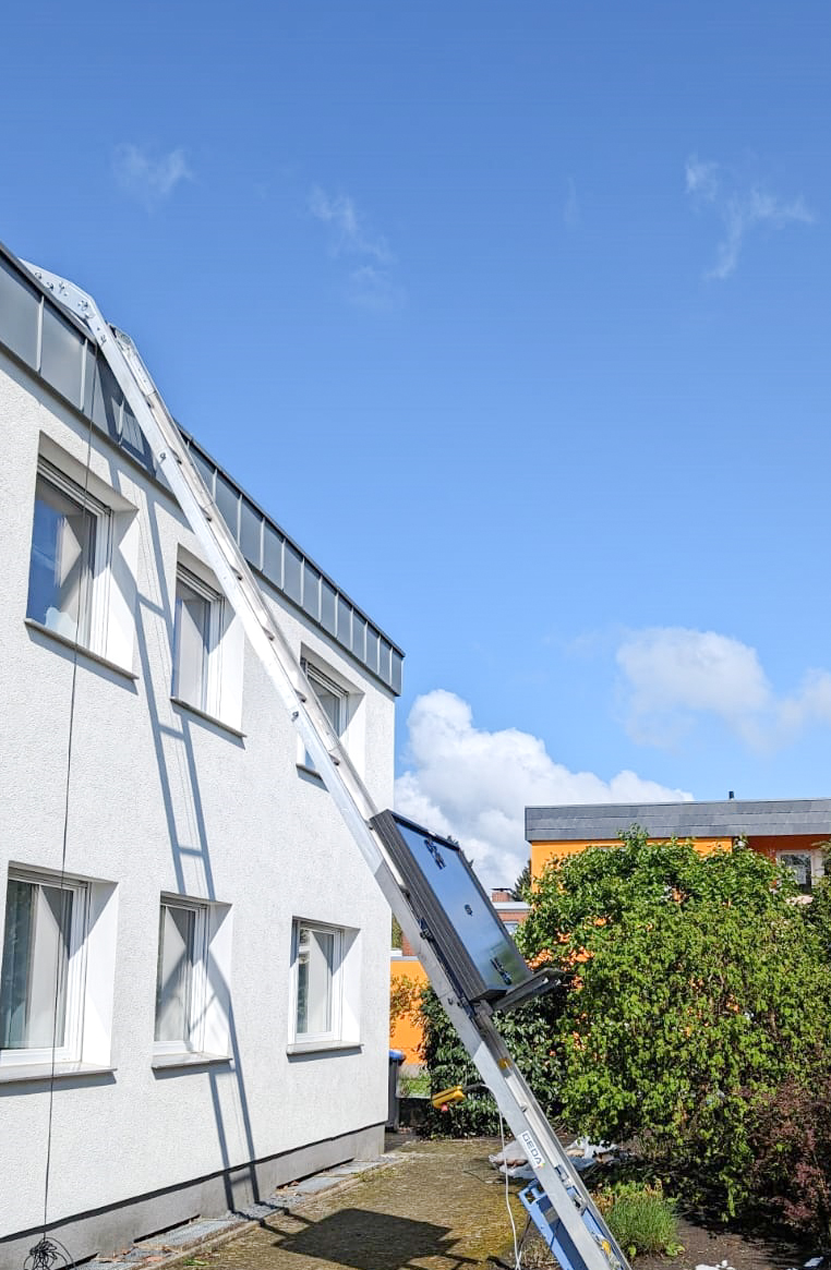 Ein Leiterlift befördert mehrere PV-Module auf ein Gebäude.