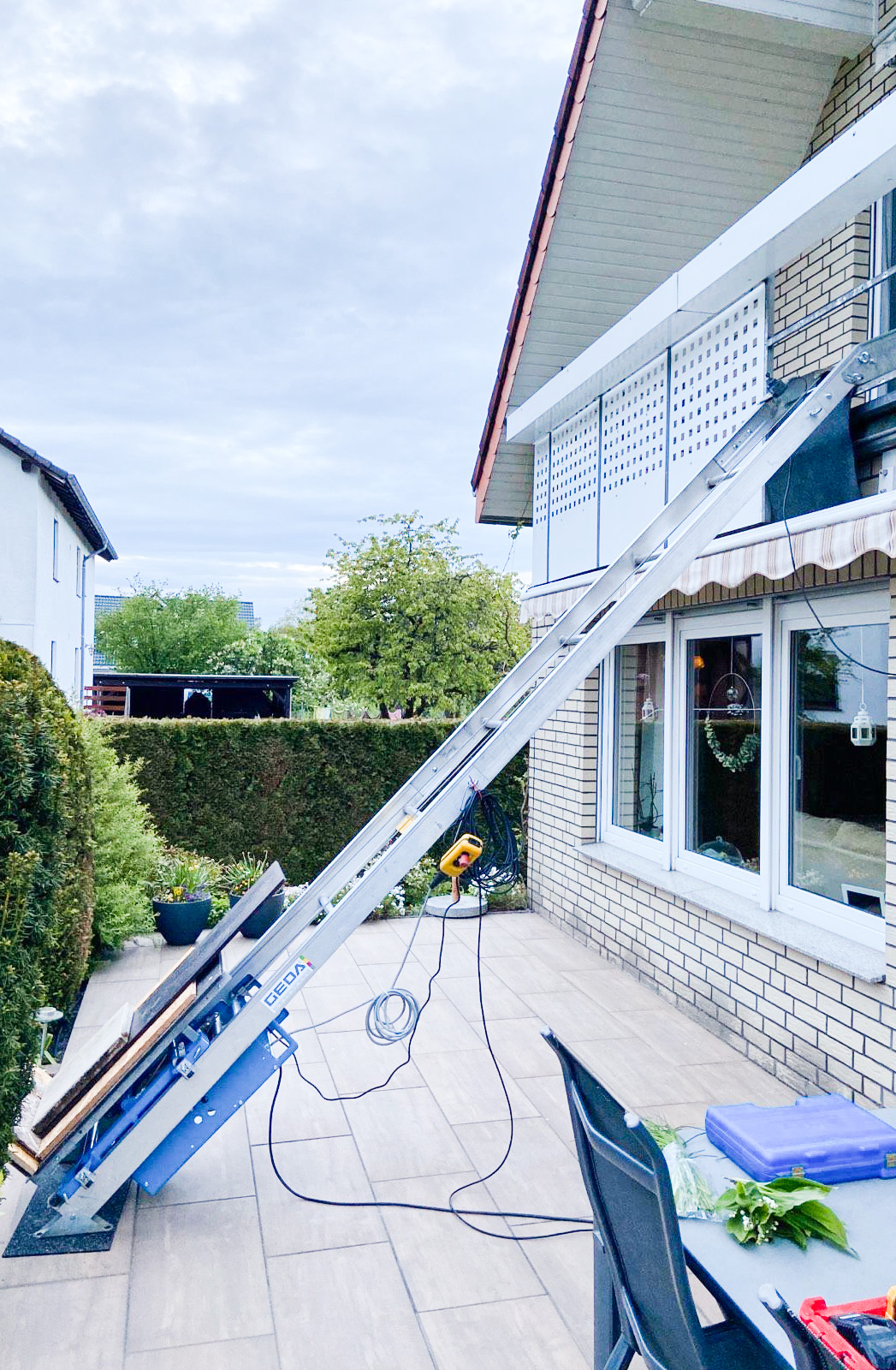 Ein Leiterlift transportiert Terrassenplatten auf einen Balkon.