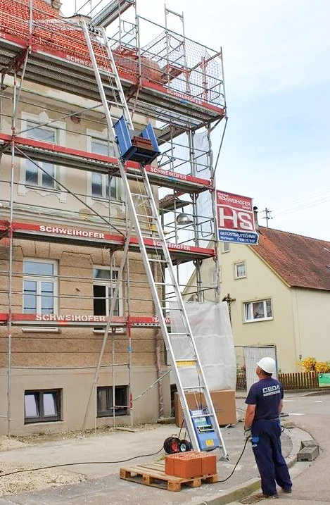 Ein Baulift transportiert Dachziegel auf das Dach eines mehrstöckigen Gebäudes.