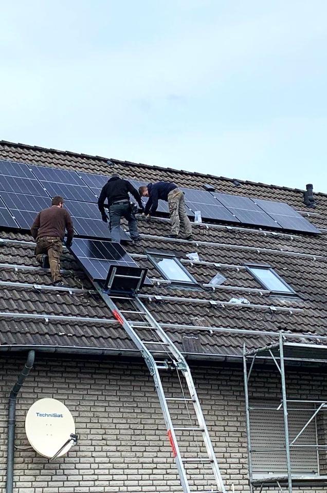 Arbeiter auf einem Hausdach mit einem Solarlift, der Solarmodule aufs Dach befördert